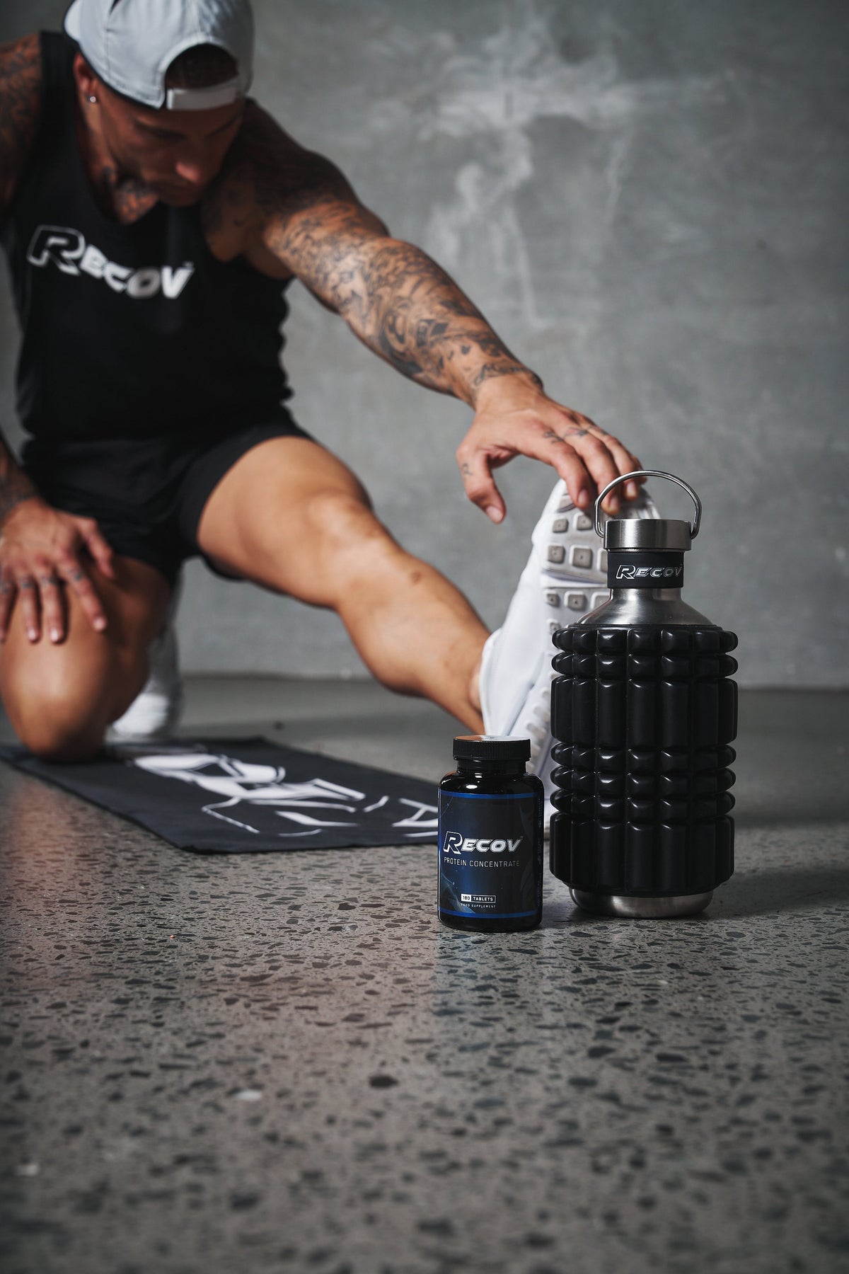 An athlete stretching on a mat beside a Recov bottle
