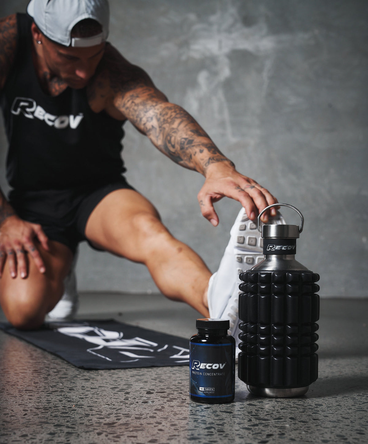 Recov Protein Concentrate on the gym floor beside a foam roller