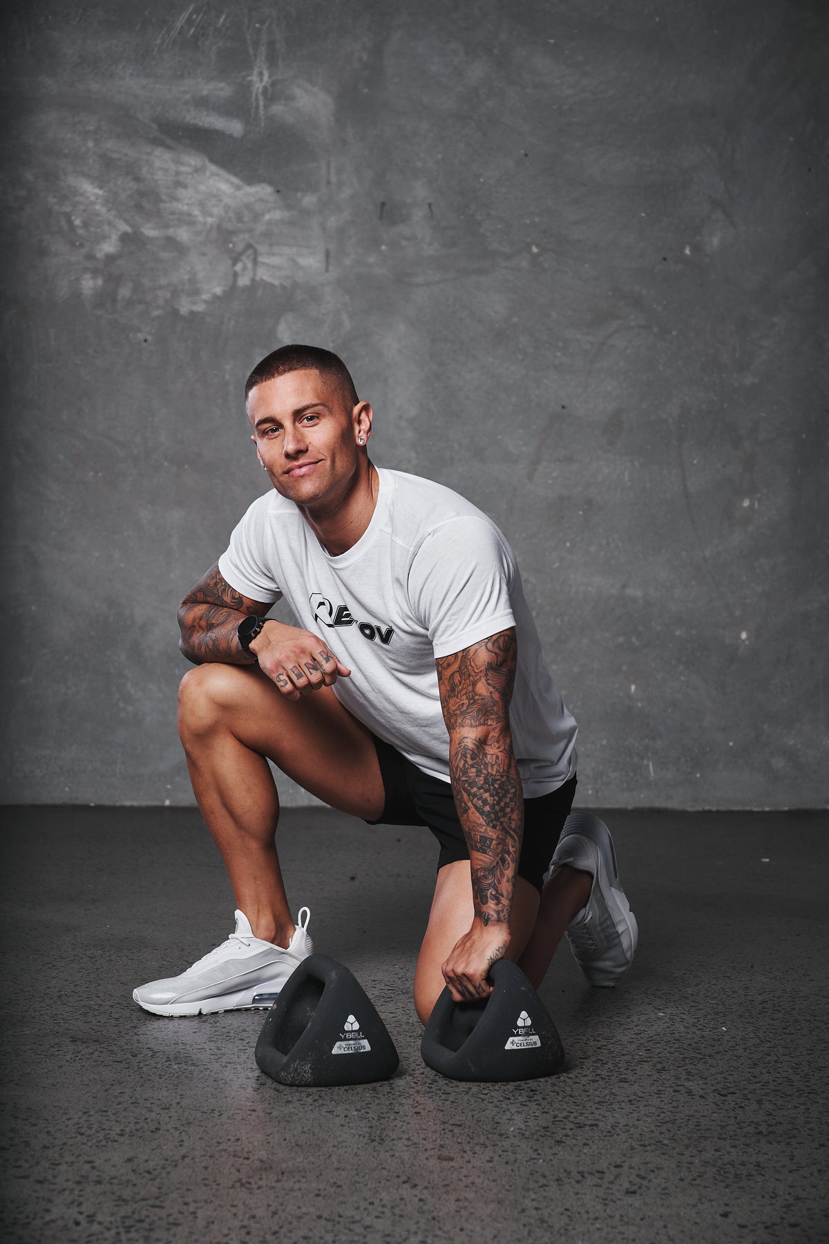 An athlete in a Recov training shirt kneeling beside training weights